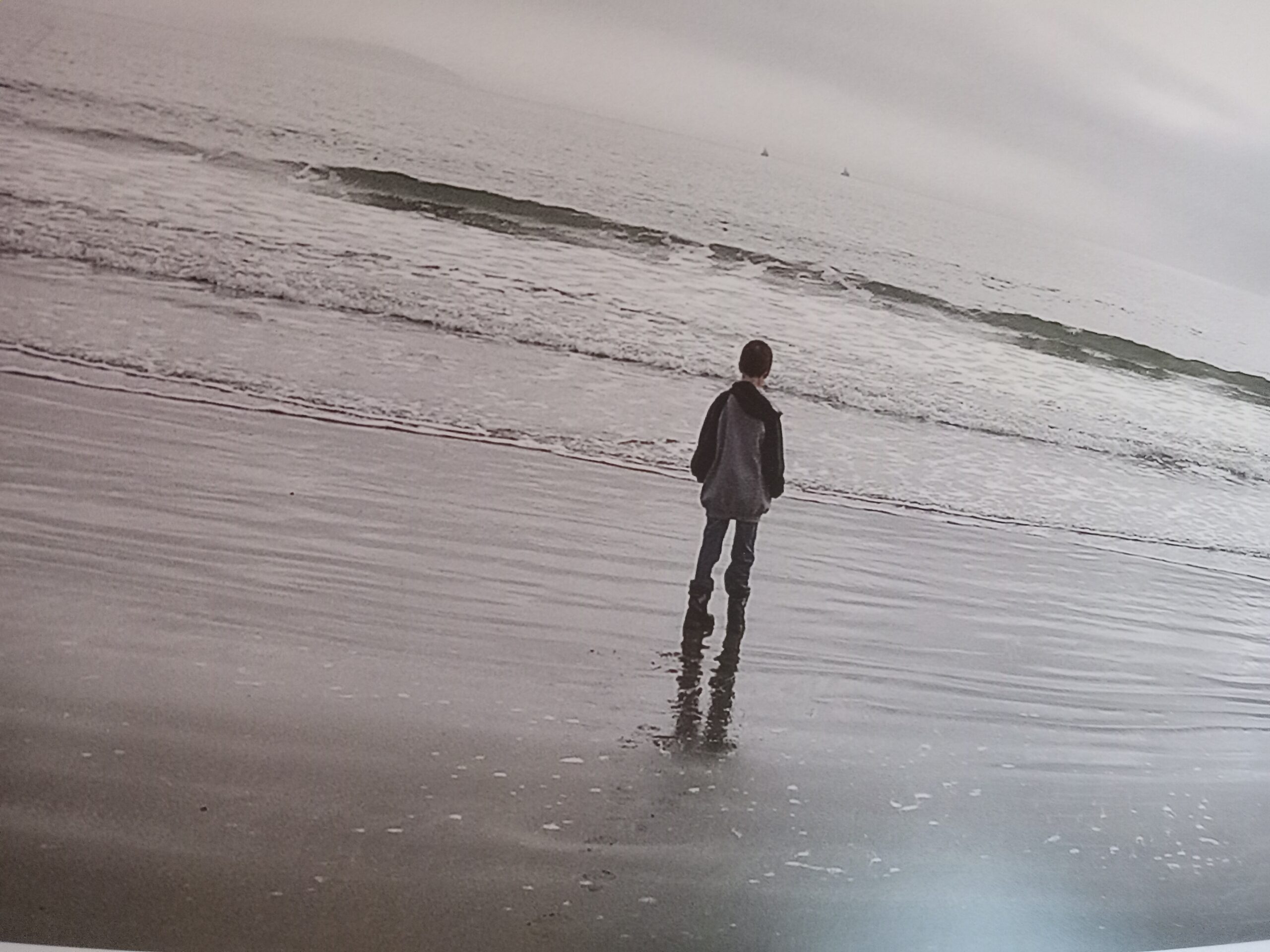 A black and white photo with a child looking towards the horizon on the beach.